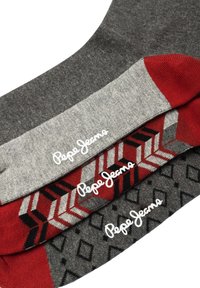 Tre paia di calzini con una combinazione di colori e fantasie: grigio con rombi neri, rosso con motivi geometrici e grigio chiaro.