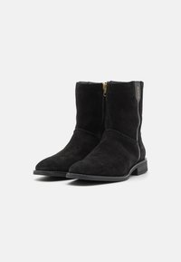 Bottines en suede noir avec un bout rond, fermeture éclair sur le côté avec quincaillerie dorée, détails de couture subtils et un petit talon empilé.