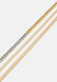 Trois colliers : une chaîne en métal argenté, une chaîne en métal doré, et une bandoulière en tissu beige texturé, chacun variant en largeur et en design.