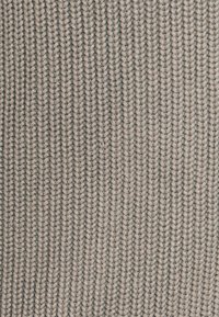 Textiltyg med ett ribbat stickat mönster i beige nyanser, med en mjuk textur och tydliga vertikala linjer.