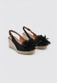Sandalias de cuña negras con un acento de flor de tela, tacón de yute trenzado y correa ajustable en el talón. Forro interior suave, diseño de punta abierta.
