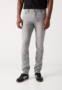 Grijze denim jeans met een slim fit, vijf zakken, subtiele slijtage en een knoopsluiting. Gepaard met zwarte sneakers met witte strepen.