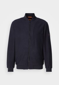 Donker marineblauwe bomberjack met ritssluiting, voorzien van een geribbelde kraag, manchetten en onderrand, en met een klein logo-opdruk op de linkermouw.