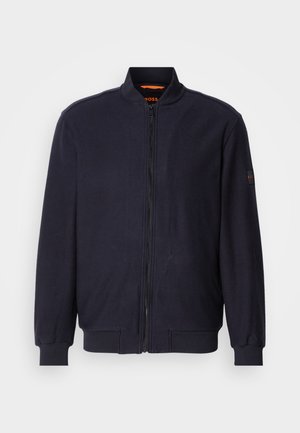 Veste bomber zippée bleu marine foncé avec col, poignets et ourlet côtelés, arborant un petit logo brodé sur la manche gauche.