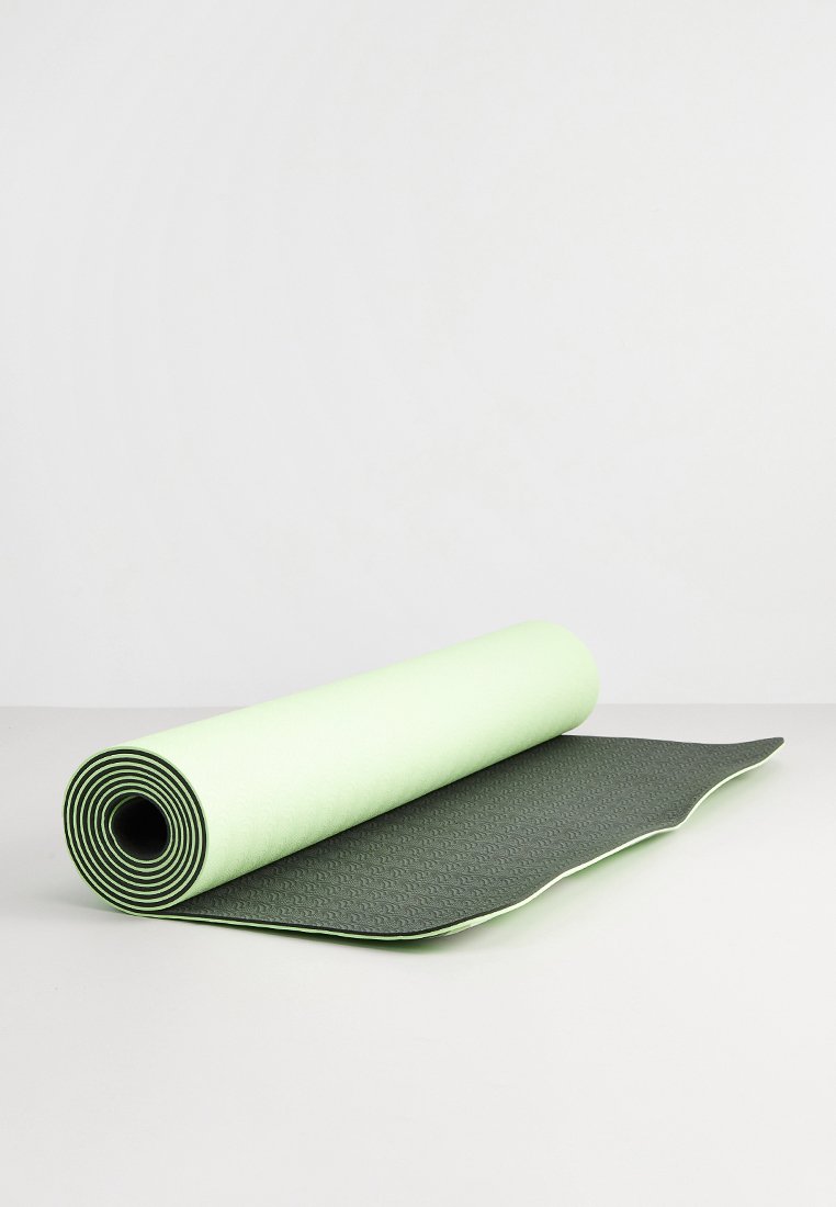 Tappetino da yoga verde e verde chiaro, arrotolato parzialmente aperto, superficie texturizzata da un lato, liscia dall'altro, con bordi arrotondati e rifinitura a contrasto.