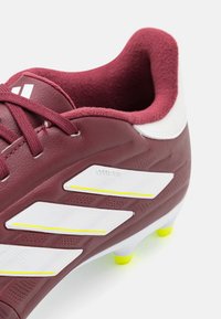Scarpa da calcio color bordeaux con accenti bianchi e gialli. Presenta una tomaia sintetica testurizzata, colletto imbottito e tacchetti conici per una migliore trazione.