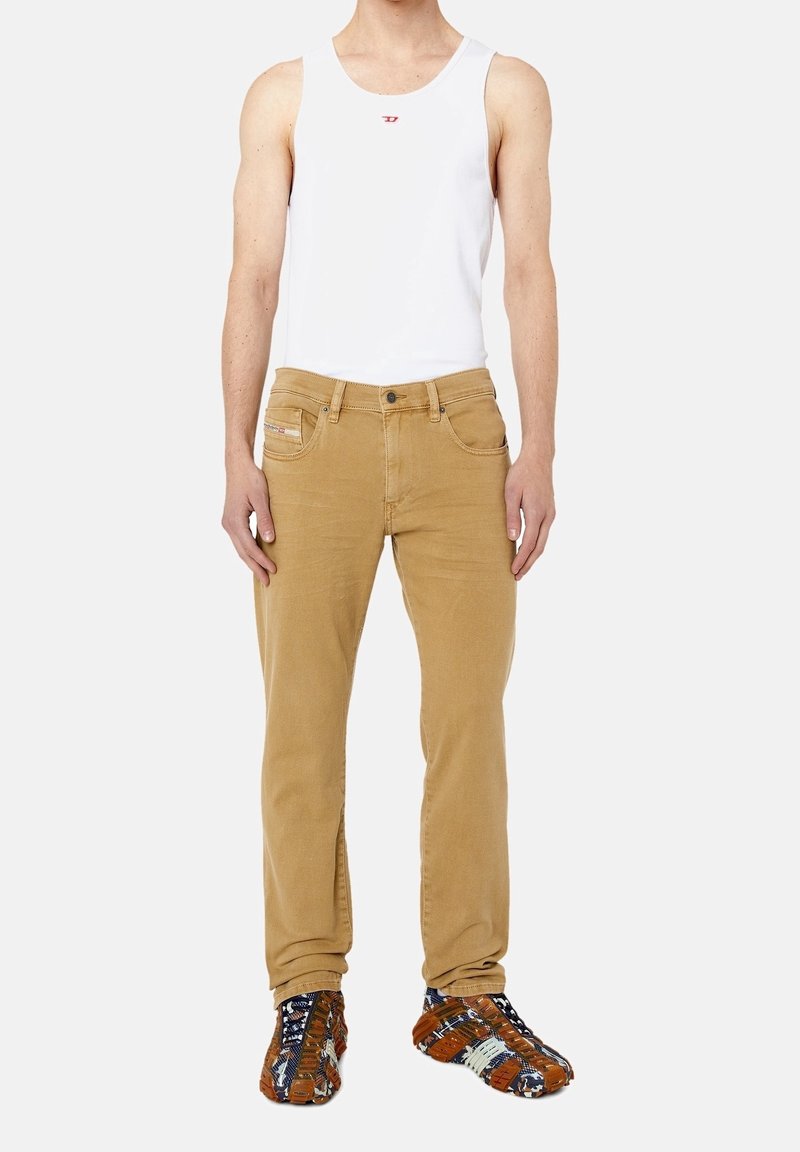 Lättvit linne med röd logotyp, i kombination med tanfärgade byxor med fickor och mönstrade flerfärgade skor.