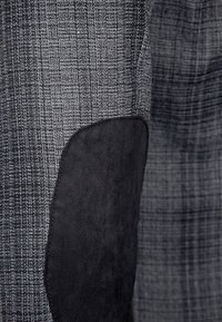 Gray textured fabric with a houndstooth pattern, featuring a black suede patch for reinforcement on one side, smooth texture overall.