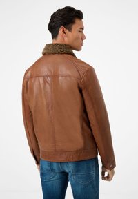 Bruine leren jas met een gestructureerde beige kraag. Heeft een aangesloten pasvorm en gestikte details op de rug. Gedirigeerd met blauwe denim jeans.
