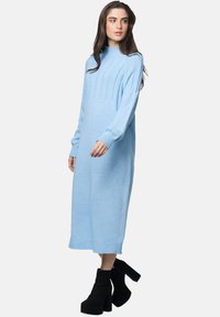 Abito lavorato a maglia azzurro chiaro con texture a coste e maniche lunghe, caratterizzato da un collo alto e una silhouette dritta, abbinato a stivali platform neri.