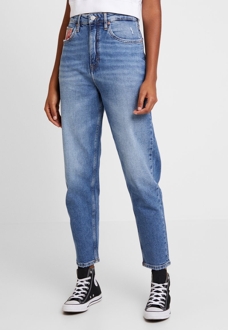 Hög midja blå denimjeans med avslappnad passform, andra med fem fickor och fransad nederkant, i kombination med svarta högsneakers.