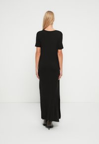 Μαύρο μάξι φόρεμα με κοντά μανίκια, απαλό ύφασμα, στρογγυλή λαιμόκοψη και πλαϊνές σκισίματα, συνδυασμένο με μποτάκια αστραγάλου για μια κομψή εμφάνιση.