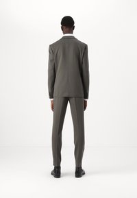 Costume gris avec blazer ajusté et pantalons, présentant un design structuré et une texture minimale, associé à des chaussures noires.