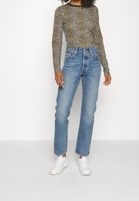 Långärmad åtsittande topp med brun och svart leopardmönster, parat med ljusblå högmidjade raka jeans och vita sneakers.