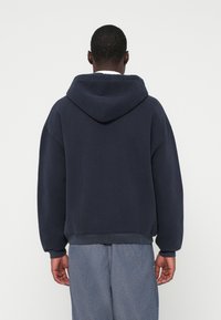 Σκούρα μπλε φουτερ με άνετη εφαρμογή, μεγάλο κουκούλα, ριμπ μανσέτες και τελείωμα, κατασκευασμένο από απαλό ύφασμα μείγματος βαμβακιού. Χωρίς ορατά σχέδια.