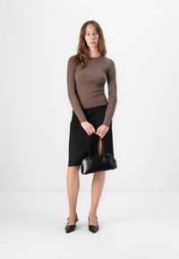Top lungo a maniche lunghe marrone a costine, gonna a matita nera con spacco laterale, borsa nera lucida e scarpe con tacco nere a punta con decorazioni a fiocco.