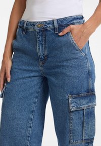 Blaue Denim-Cargohosen mit hoher Taille, seitlichen Taschen und kontrastierenden Nähten. Der Stoff ist strukturiert und strapazierfähig.