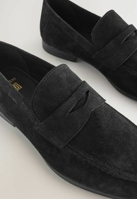 Schwarze Wildleder-Slipper mit einem genähten Design und einem auffälligen Akzentumschlag. Die Textur ist weich mit einer glatten Sohle für angenehmen Tragekomfort.