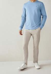 Felpa azzurro chiaro con collo a giro e maniche lunghe, abbinata a pantaloni beige e sneakers bianche. Design semplice e casual, senza motivi.