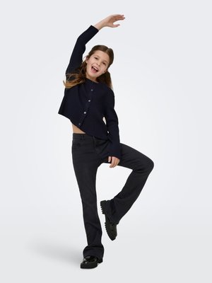 Navy ribbed long-sleeve cardigan with buttons, paired with dark denim flared jeans and black platform shoes, posing with one arm raised.