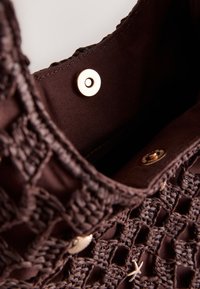 Brown woven bag with open top showing dark fabric interior and metallic snap button closure.