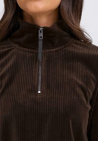 Bruine corduroy rits-top met een hoge kraag. Beschikt over verticale ribbels en een metalen rits, ontworpen voor comfort en warmte.