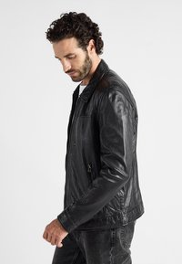 Zwarte leren jas met een gladde textuur, staande kraag en ritssluitingen aan de voorkant. Bevat ritstasjes aan de zijkanten en heeft een getailleerde pasvorm.