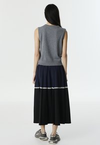Graues ärmelloses Strickoberteil kombiniert mit einem langen marineblauen Rock mit schwarzen Akzenten und einem Spitzenbesatz, getragen mit grauen Sportschuhen.