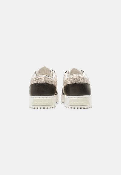 Paire de baskets blanches avec des panneaux de talon noirs et un motif texturé, vues de dos sur un fond blanc uni.