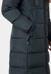 Mørkegrøn pufferjakke med quiltede sektioner, lynlåslommer og ribbet strikmanchetter. Har en lille svensk flagaccent nær lommen.