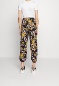 Spodnie w kwiatowy wzór na czarnym tle; zdobione złotymi okrągłymi akcentami i elastycznymi mankietami. Noszone z białym t-shirtem i czarnymi trampkami.