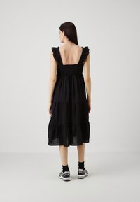 Rochie neagră, cu fuste în straturi, bretele volănașe, spate pătrat și un material ușor. Modelul poartă adidași și șosete până la gleznă.