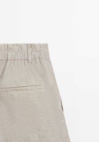 Beżowo-białe spodnie w paski z elastycznym paskiem w talii i jedną kieszenią na plecach na białym tle.