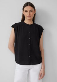 Blouse sans manches noire avec un col haut, détails plissés aux épaules et fermeture à boutons à l'avant, fabriquée dans un tissu texturé.