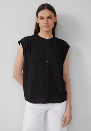 Schwarze ärmellose Bluse mit hohem Kragen, gefalteten Schulterdetails und Knopfverschluss vorne, aus einem strukturierten Stoff gefertigt.