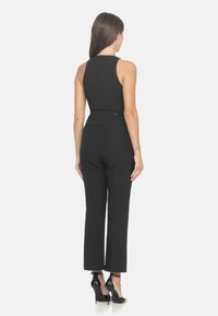 Giubbotto nero aderente con design senza maniche, pantaloni affusolati e vita definita. Presenta una superficie liscia e una silhouette elegante.