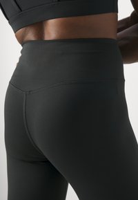 Magas derekú fekete leggings rugalmas anyagból, sima felületű és lapos varrásokkal a kényelem és a tartósság érdekében.