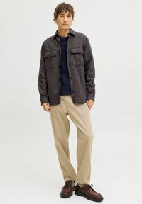 Tumehall teksuuriga särkjakk kahe eesmise taskuga, sobitatud tumesinise kampsuni ja beežide pükstega. Välimuse lõpetavad pruunid paeltega kingad.