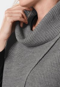 Grauer Strickpullover mit einem Cowl-Neck und einem strukturierten Muster. Der Stoff scheint weich und flexibel zu sein und zeigt ein lockeres Design um den Hals.