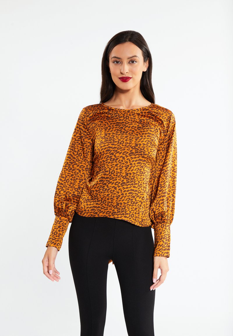 Een top met luipaardprint in oranje en bruine tinten, met lange ballonmouwen en een diepe halslijn, gecombineerd met zwarte legging.