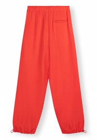 Rode, losse broek gemaakt van lichtgewicht stof. Heeft een elastische tailleband en een trekkoord bij de enkels. Inclusief een klein achterzakje.