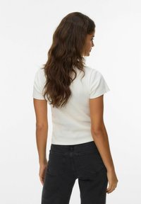 Tætsiddende hvid ribbet kortærmet top med rund hals, parret med højtaljede sorte jeans med baglommer. Enkel og ren design.