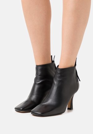 Stivaletti neri in pelle, con punta affusolata, tacco sottile e superficie liscia. Presentano una chiusura con zip e un design sottile e minimalista.