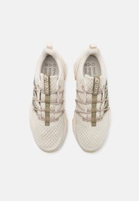 Zapatos deportivos ligeros en malla beige con acentos verdes. Cuentan con cordones elásticos y una suela texturizada para agarre y flexibilidad.