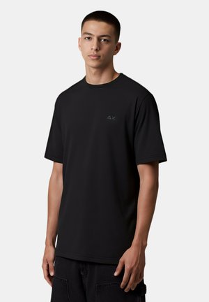 T-shirt nera a maniche corte in tessuto morbido con scollo rotondo e una piccola accentatura con logo verde sul lato sinistro. Design semplice.