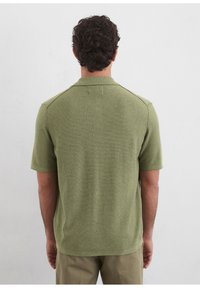 Short-sleeve polo in textured olive green fabric with a collar and subtle horizontal stripe detailing on the back and shoulders.