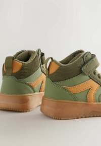Baskets montantes en vert olive et beige, avec une tige texturée, une sangle à boucle auto-agrippante et une semelle en caoutchouc qui assure une bonne traction.