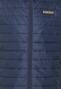 Marineblauer Puffer-Westen mit horizontaler Steppung, Frontreißverschluss und einem kleinen strukturierten Logo-Patch auf der Brust. Leichtes, wasserabweisendes Material.