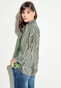 Blusa a righe verdi e bianche con maniche lunghe, colletto con bottoni e vestibilità comoda, abbinata a jeans in denim blu.