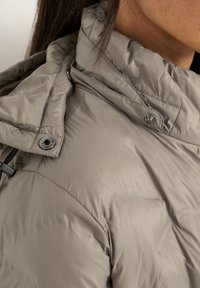 Gevoerde jas met een hoge kraag, in lichtbeige kleur, met een zachte textuur en zilveren hardware-details op de kraag en sluiting.